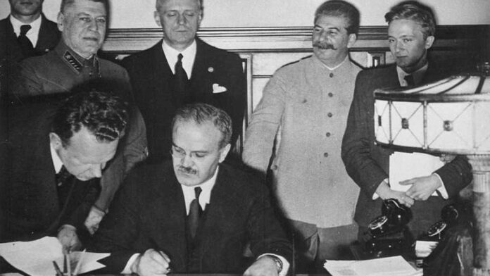 Foreign Minister Vyacheslav Molotov signs the pact. Behind him are Ribbentrop and Stalin